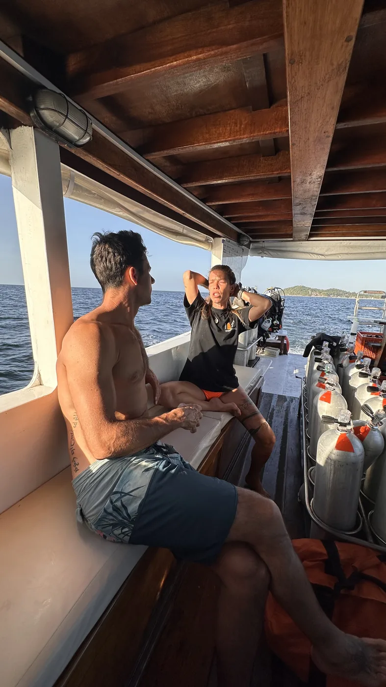 An instructor giving a pre-dive briefing on the boat next to a row of clean, racked tanks, Koh Lipe